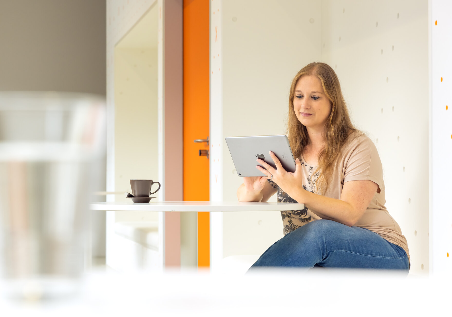 Das Foto zeigt eine Frau mit einem Tablet in der Hand an einem Tisch sitzend.