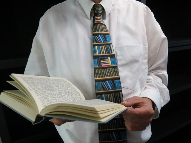 Mann mit aufgeschlagenem Buch in seinen Händen und Krawatte mit Buchregalmuster